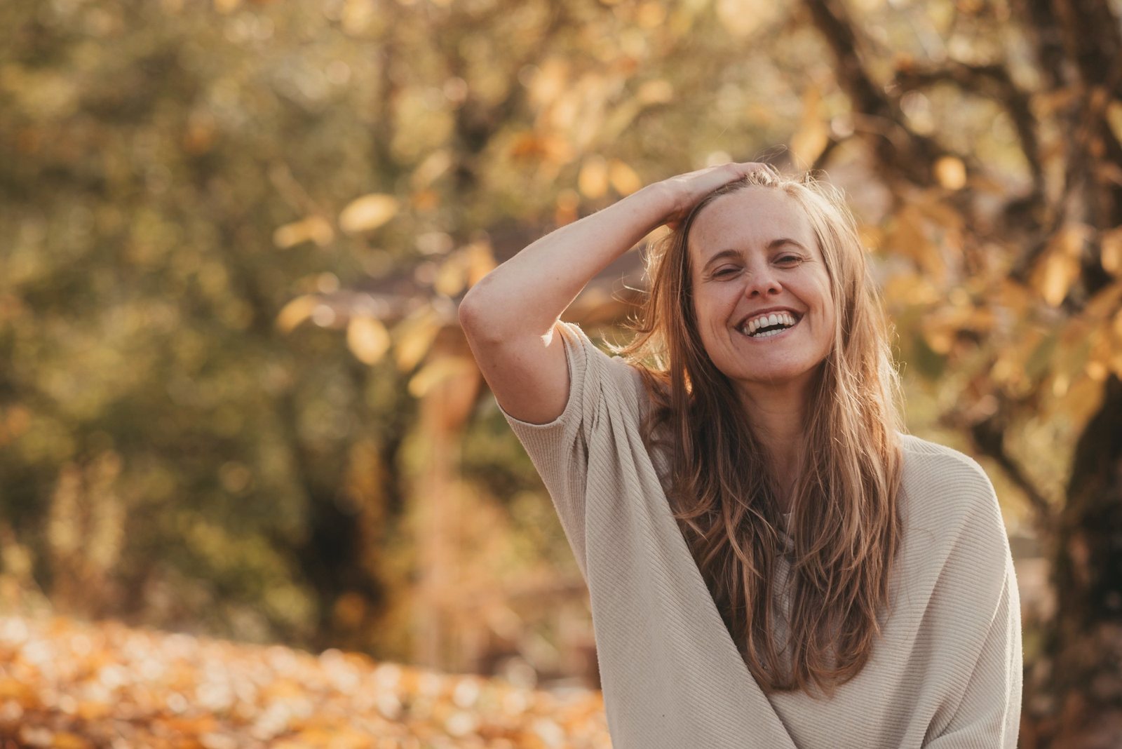 Suyana laughing, one hand in her hair, autumn leaves glowing behind her